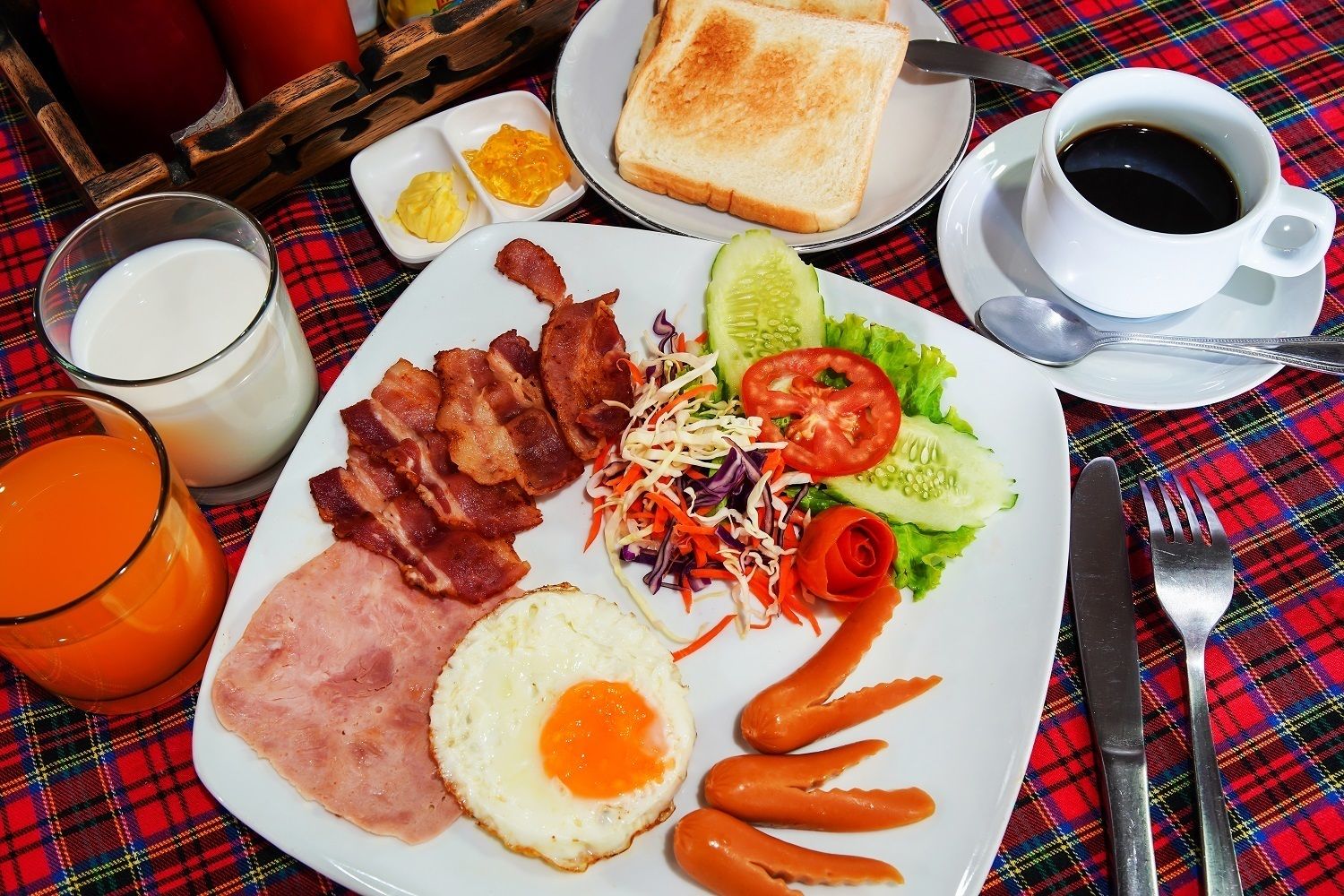 A breakfast plate with bacon, ham, eggs, and vegetables, along with toast, a glass of orange juice, and a cup of coffee.