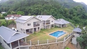 Ein großes, mehrgeschossiges Haus mit Swimmingpool, umgeben von üppiger Vegetation und Hügeln.