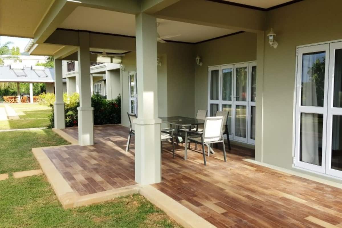 Un patio cubierto con terraza de madera, una mesa con sillas y grandes puertas correderas de cristal.