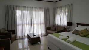 Ein Hotelzimmer mit einem Bett, einem Sofa, einem Sessel, einem Tisch und großen Fenstern mit durchsichtigen Vorhängen.