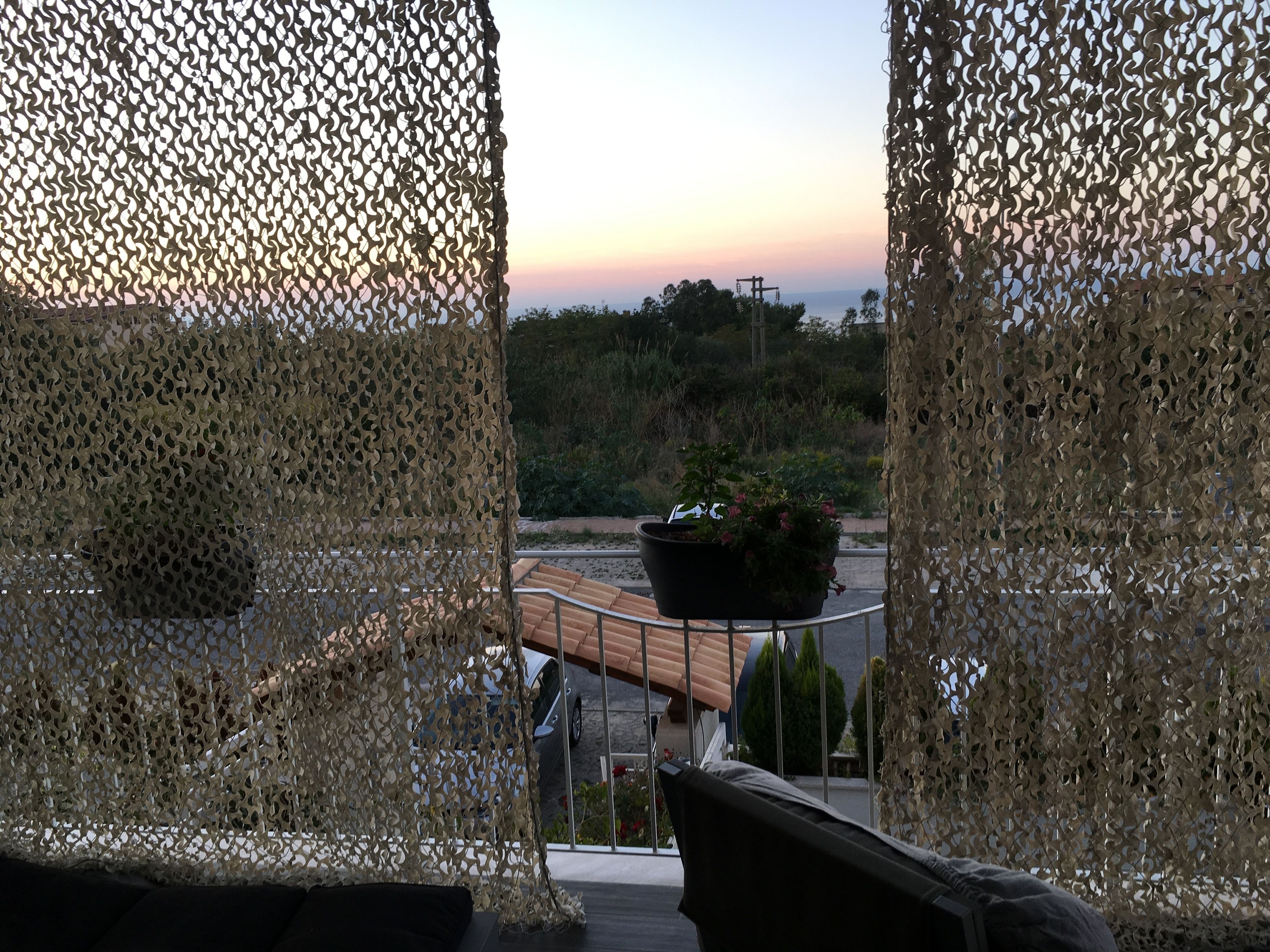 Ein Balkon mit Blick auf einen Sonnenuntergang, einem Blumentopf und einem Geländer.