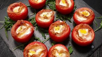 Una bandeja de tomates rellenos con un huevo escalfado, adornada con hierbas, sobre una tabla de pizarra.