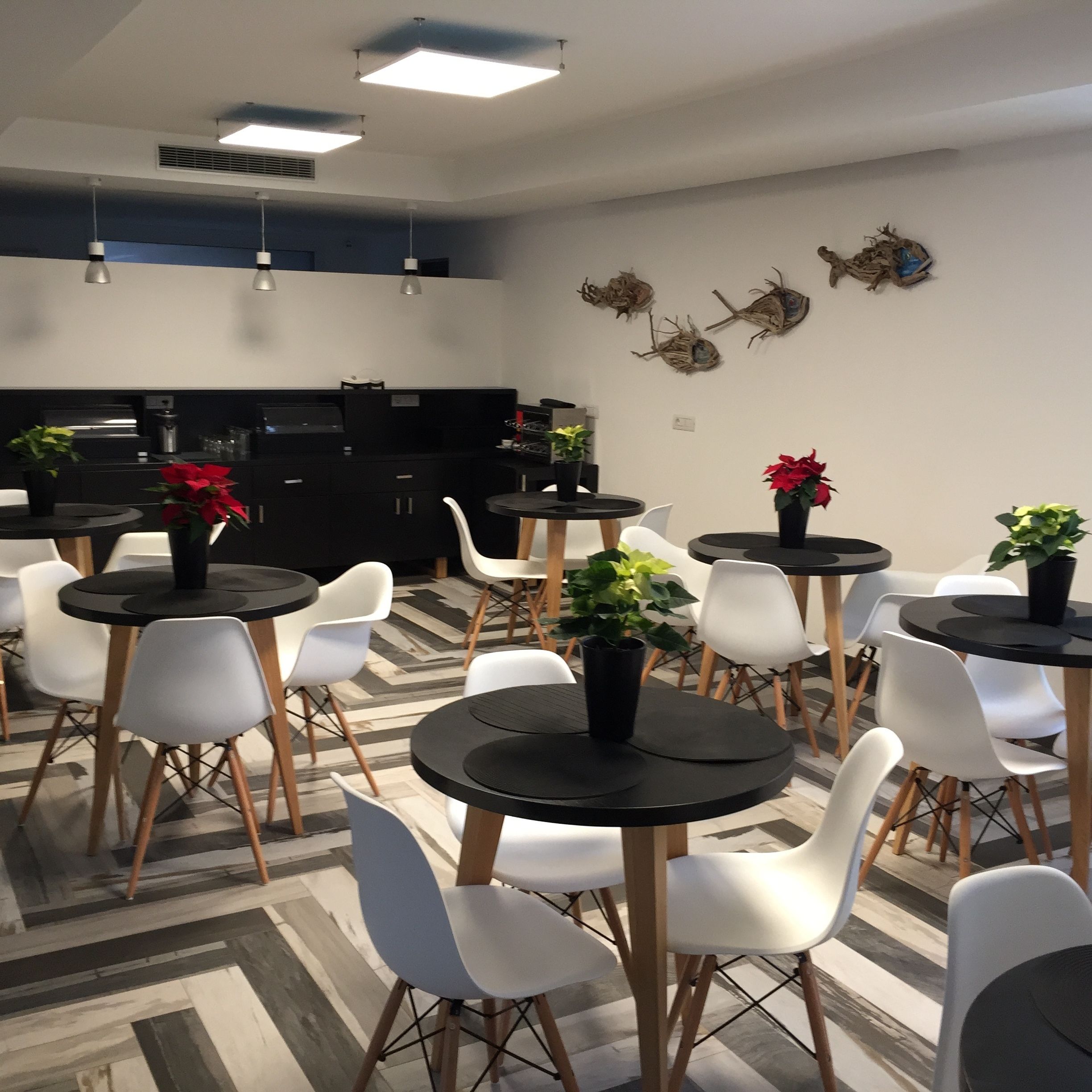 A modern dining area with round tables and white chairs, a kitchen in the background, and decorative wall art.