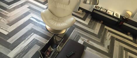 A modern living room with a white leather armchair, a black ottoman, and a patterned floor.
