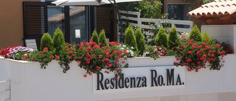 Un letrero que dice "Residenza Ro.Ma." con una pared blanca, flores rojas y un paraguas blanco.