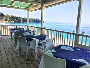 An outdoor dining area with tables and chairs, overlooking a beach and the sea. - Residenza RoMa (Tropea)
