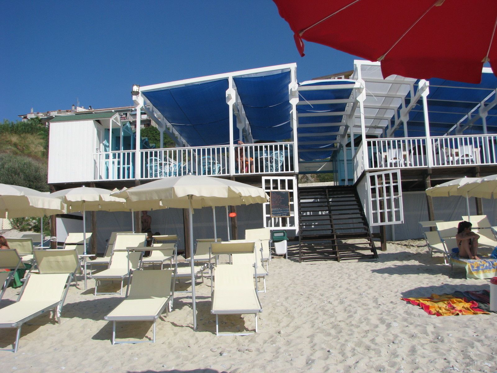 A beachside building with multiple levels, outdoor seating, and umbrellas.