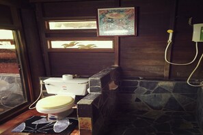 A bathroom with a toilet, a shower, and a stone wall. - Baan Parimtarn Kanchanaburi (Kanchanaburi)