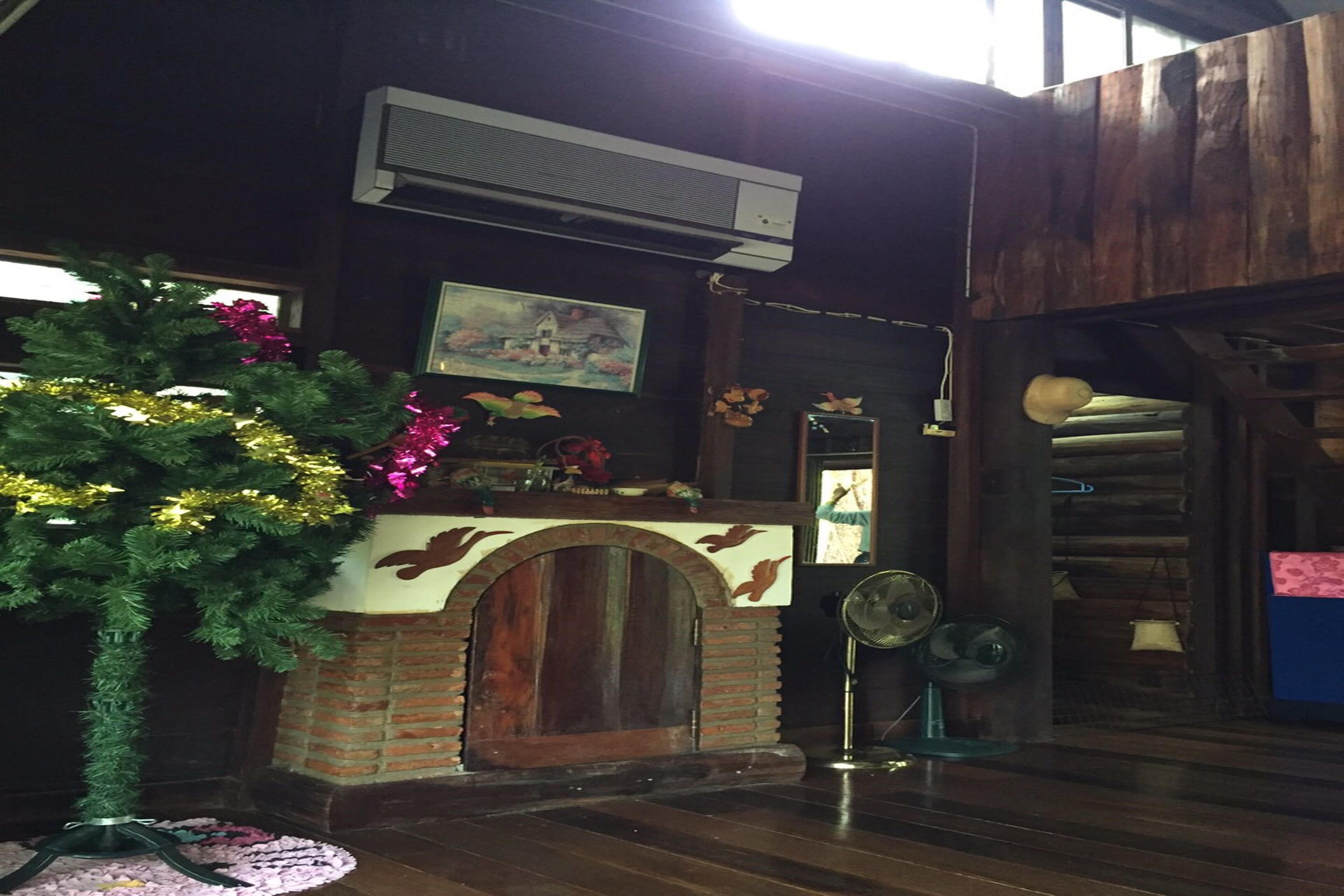 A rustic room with a brick fireplace, a small tree decorated with tinsel, and a painting on the wall.