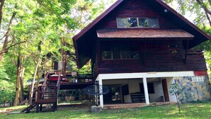 A two-story wooden cabin with a balcony, surrounded by trees.