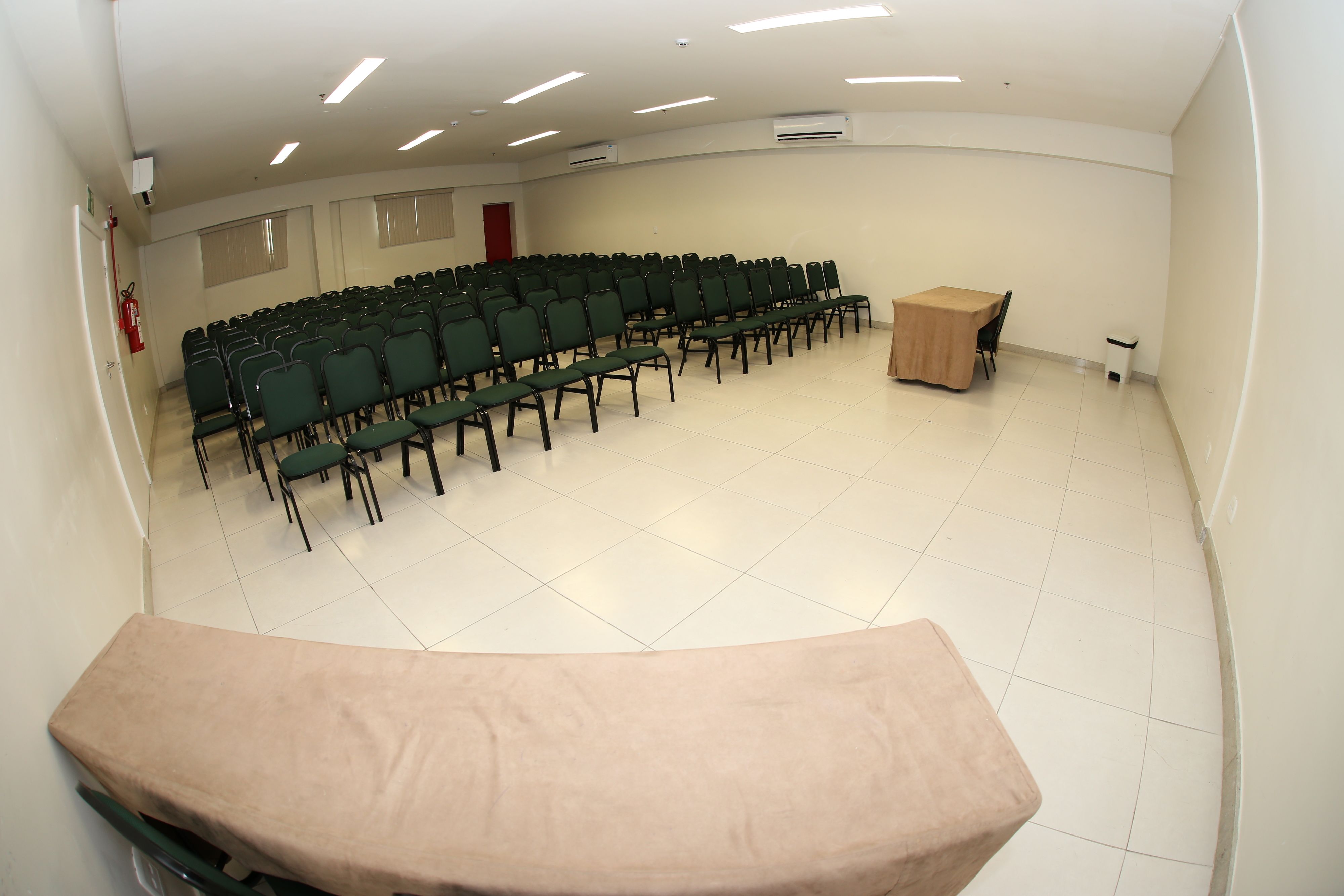 A conference room with rows of chairs, a table, and an air conditioning unit on the wall.