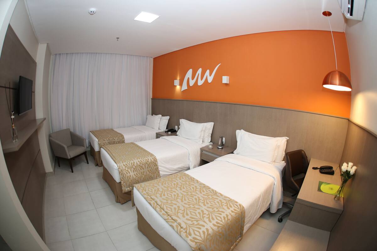 Een hotelkamer met twee bedden, een bureau met telefoon en een vaas met bloemen, en een televisie aan de muur.