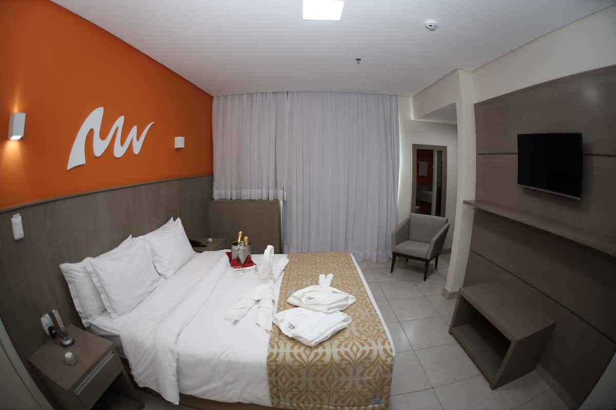 Een hotelkamer met een bed, nachtkastje, televisie en stoel.