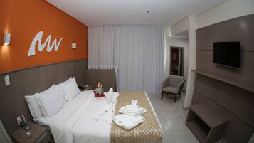 A hotel room with a bed, a nightstand, a TV, and a chair.