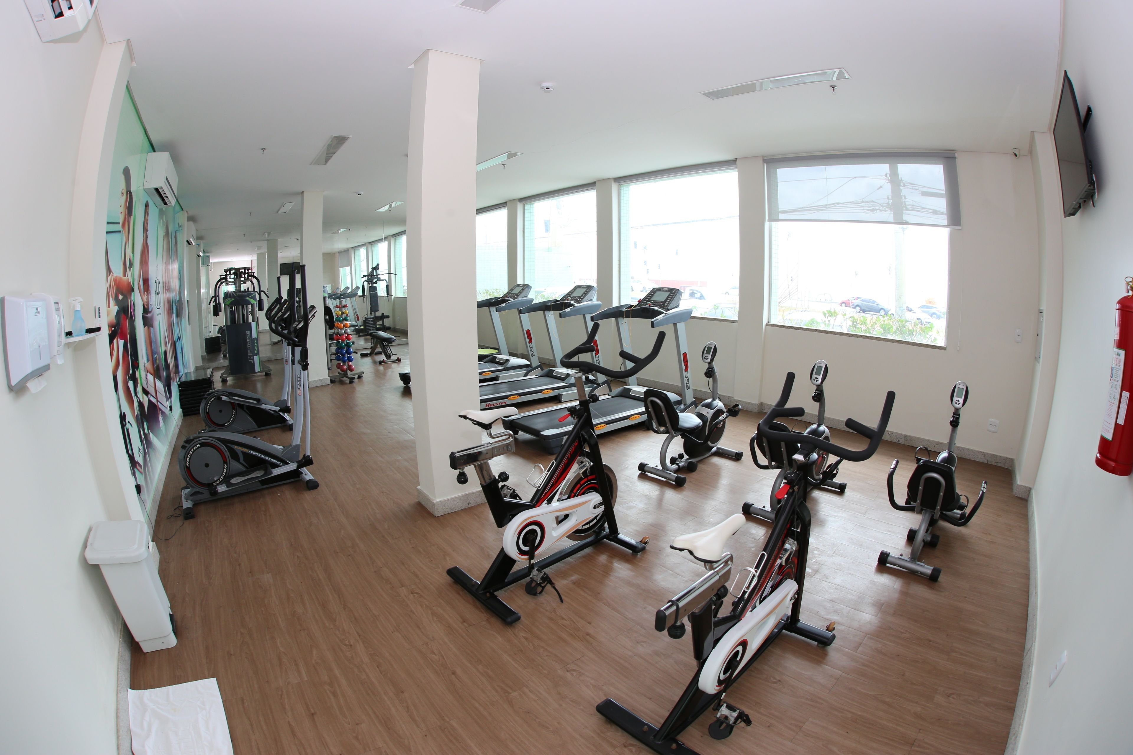 Une salle de sport équipée de nombreux appareils d’exercice, dotée de grandes fenêtres et d’un intérieur propre et moderne.
