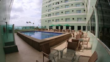 A hotel pool area with a rectangular pool, lounge chairs, and a glass table.