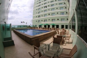 Zona de piscina de hotel con una piscina rectangular, sillas de descanso y una mesa de vidrio.