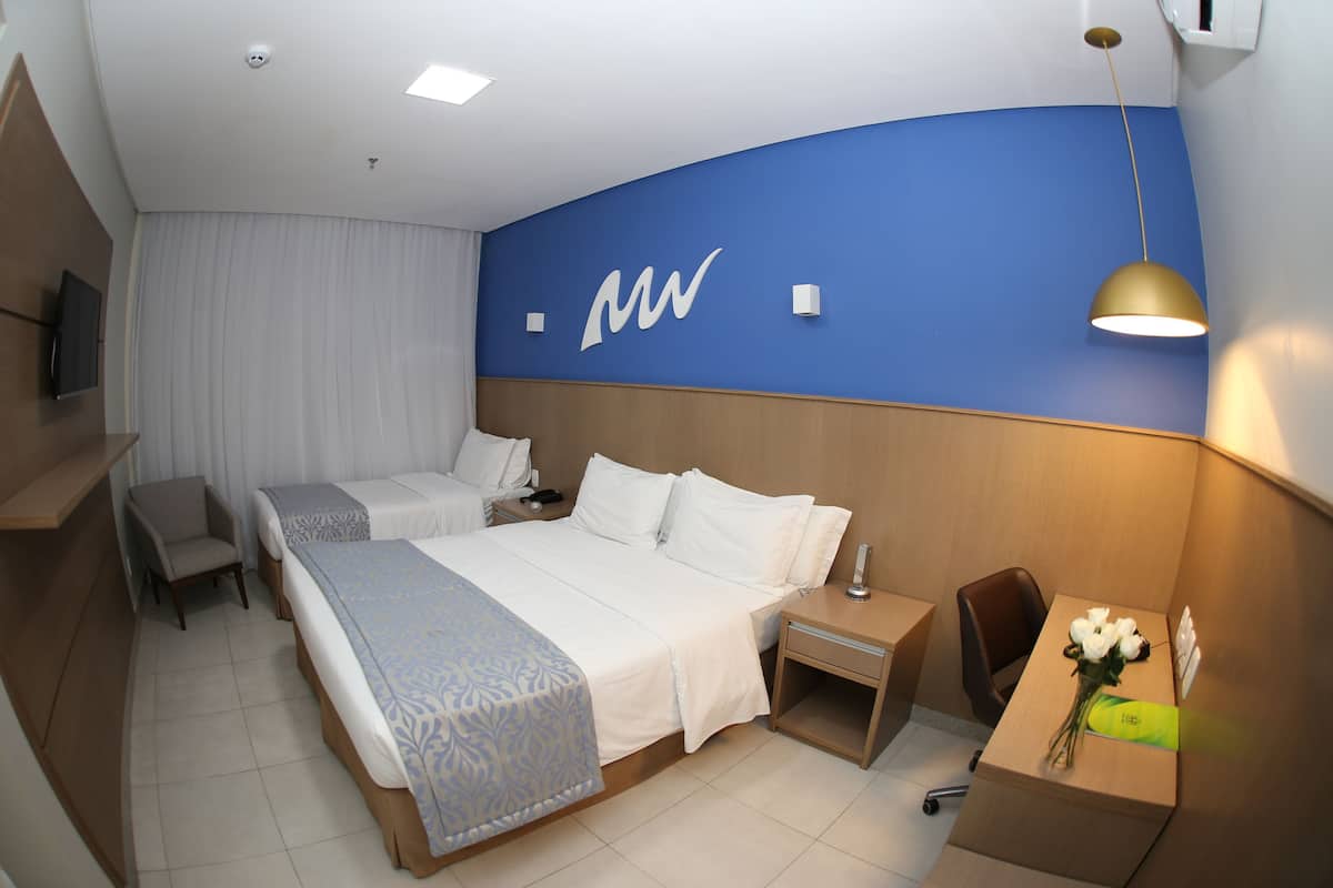 Een hotelkamer met een groot bed, een bureau met stoel, een kleine tafel met bloemenvaas, en een aan de muur bevestigde televisie.
