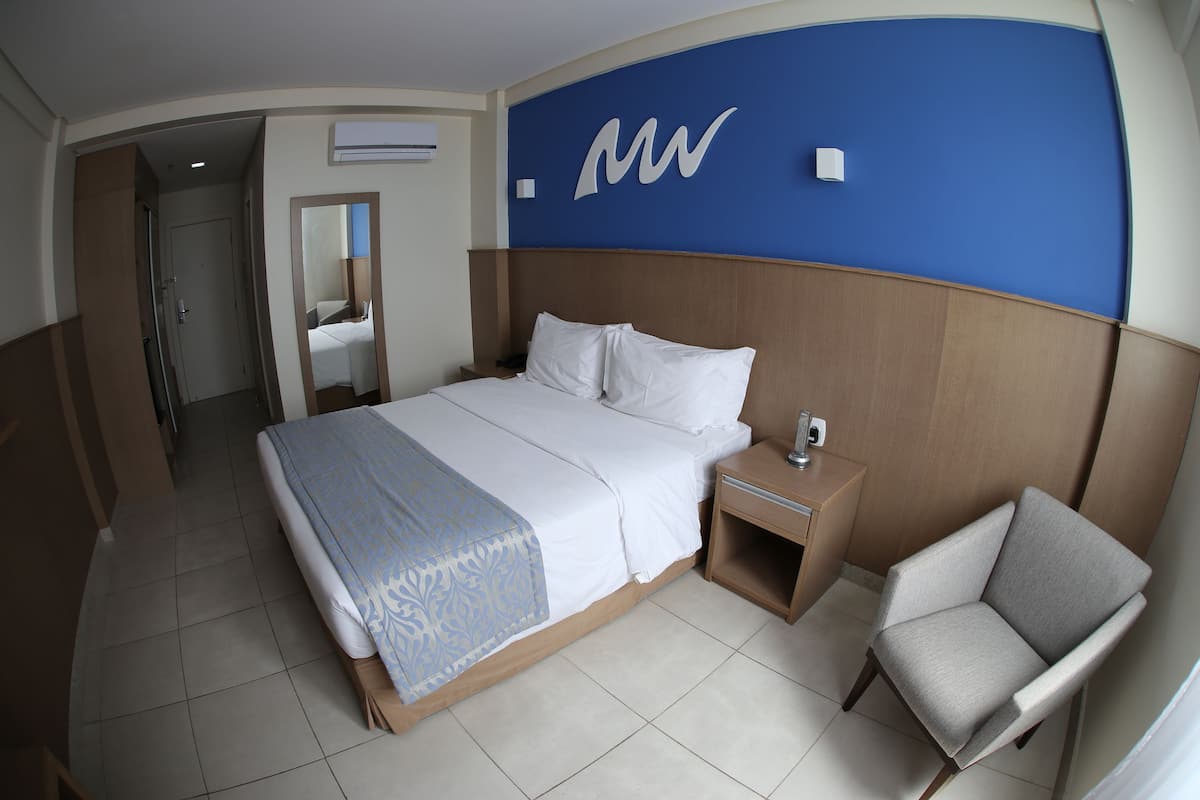 Een hotelkamer met een groot bed, een nachtkastje, een stoel en een blauwe accentmuur met een logo.