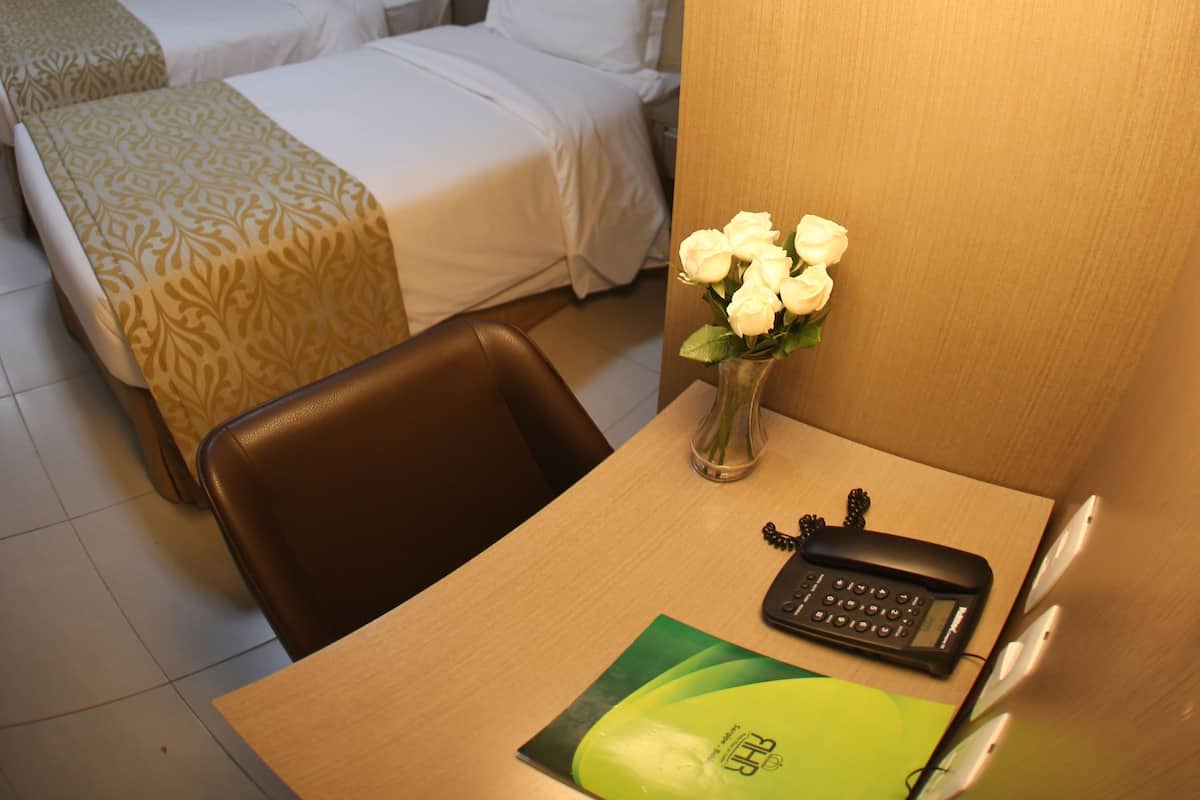 Hotelkamer met twee bedden, een bureau met telefoon, een vaas met bloemen en een grote ronde lamp.
