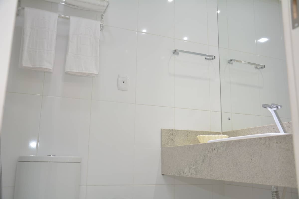 Een badkamer met witte tegels, een toilet, een wastafel met spiegel en twee handdoeken aan een rek.