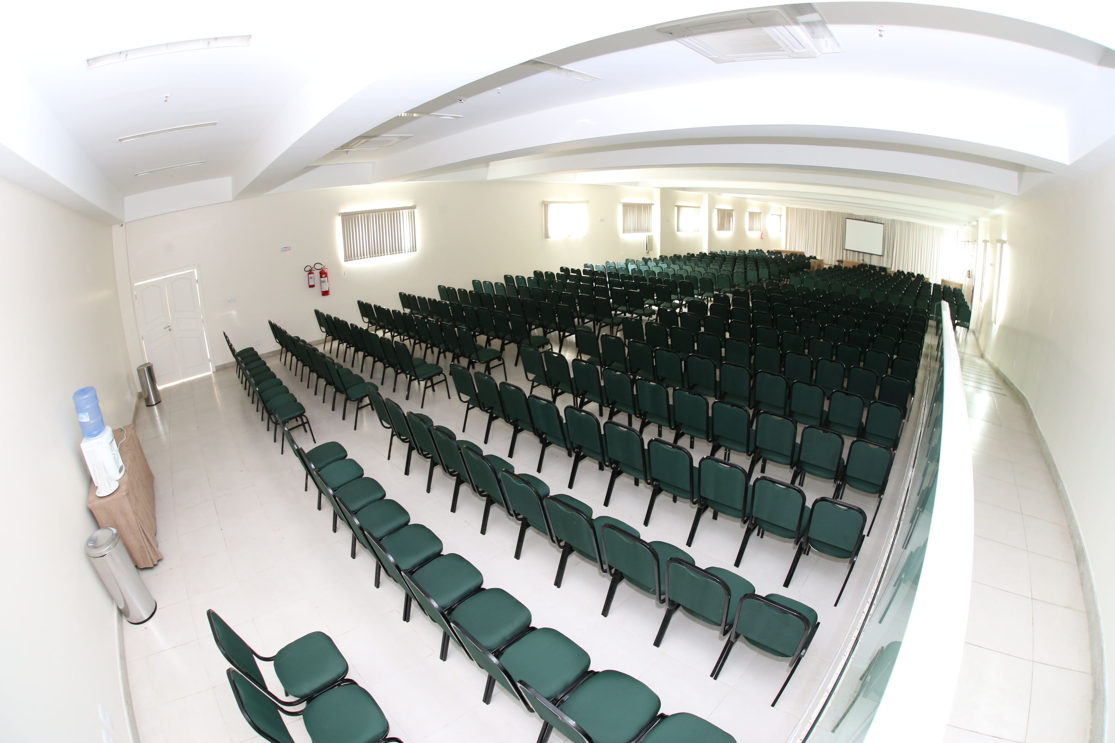 A conference room with rows of green chairs, a white ceiling, and a projector screen.
