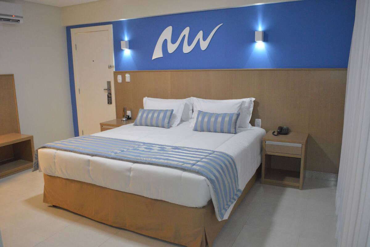 Een hotelkamer met een groot bed, een houten hoofdeinde, een nachtkastje met een telefoon en een wandlamp.