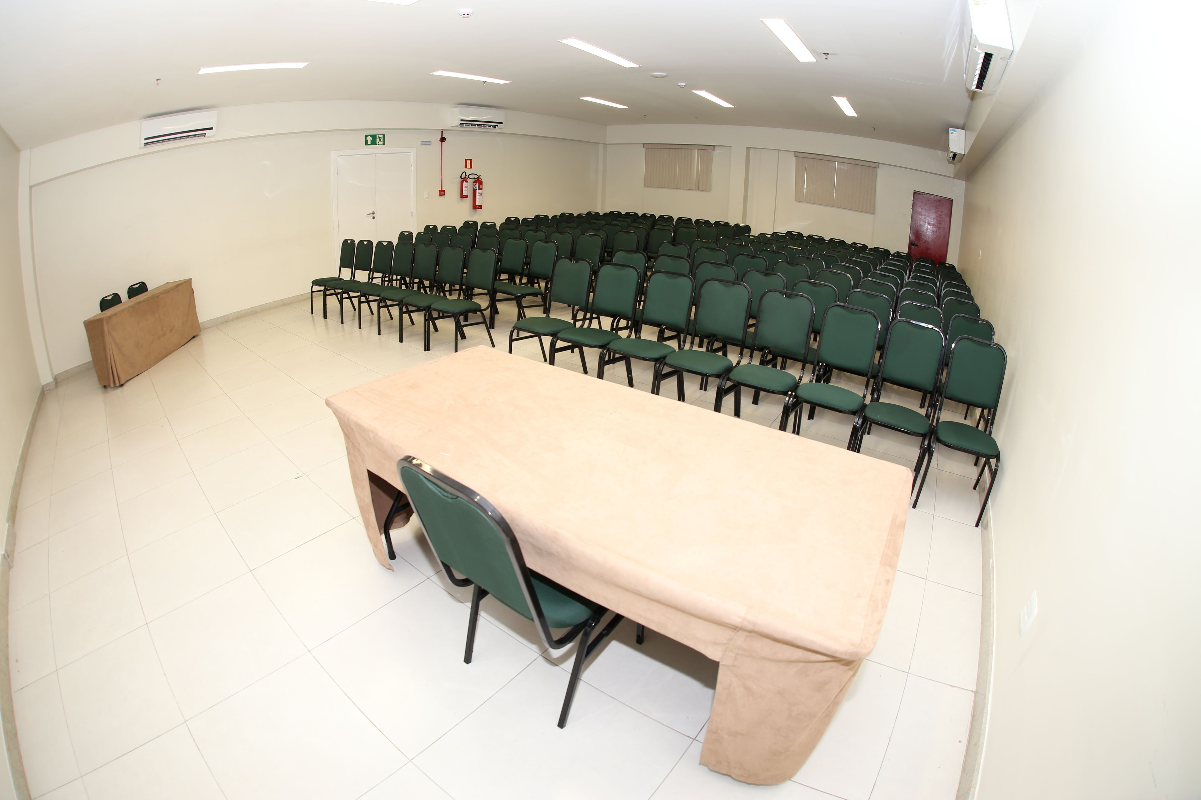 Ein Konferenzraum mit langem Tisch, Reihen von Stühlen, Klimaanlagen und einem Feuerlöscher an der Wand.
