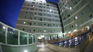 Um hotel com vários andares, piscina, área de estar externa e espaço envidraçado.