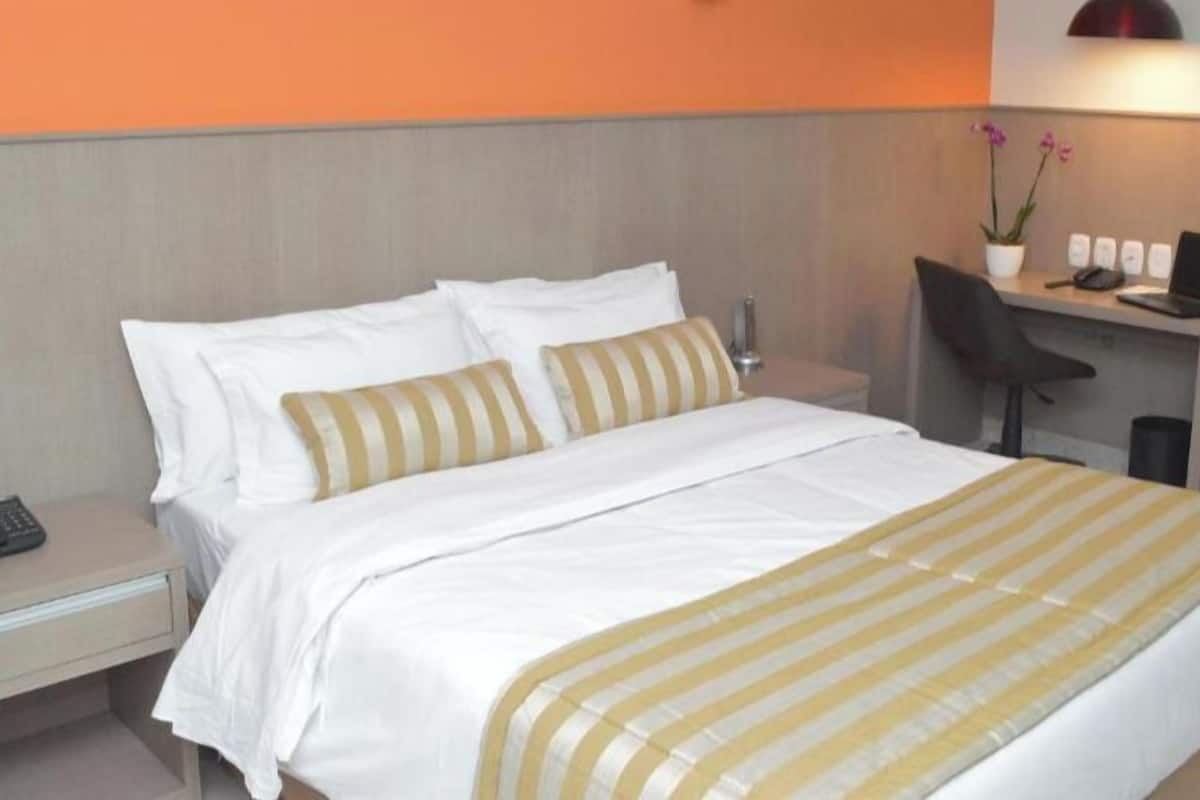 Een hotelkamer met een bed, een bureau met een laptop, een stoel en een klein tafeltje met een telefoon.