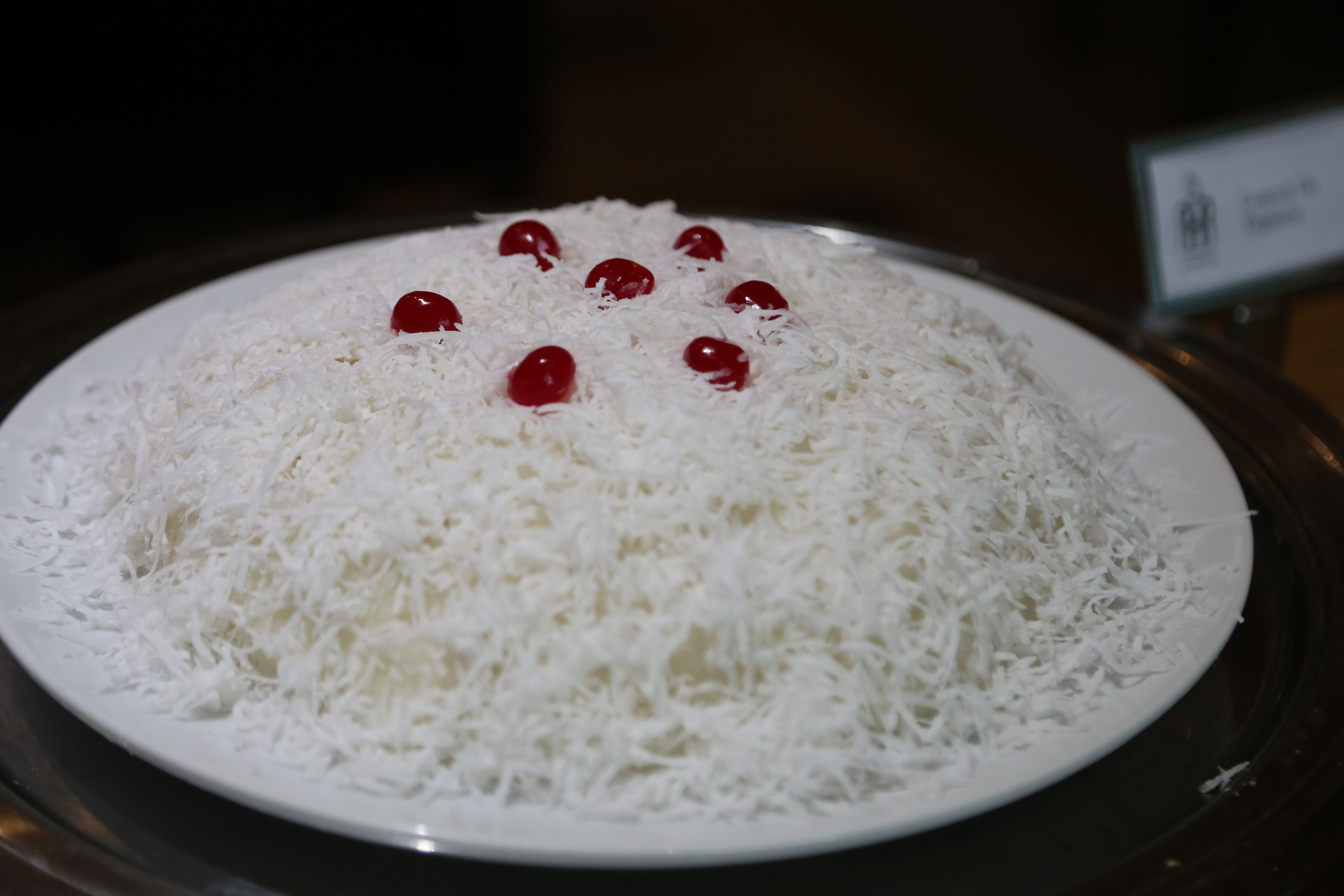 A plate of shredded coconut with red cherries on top.