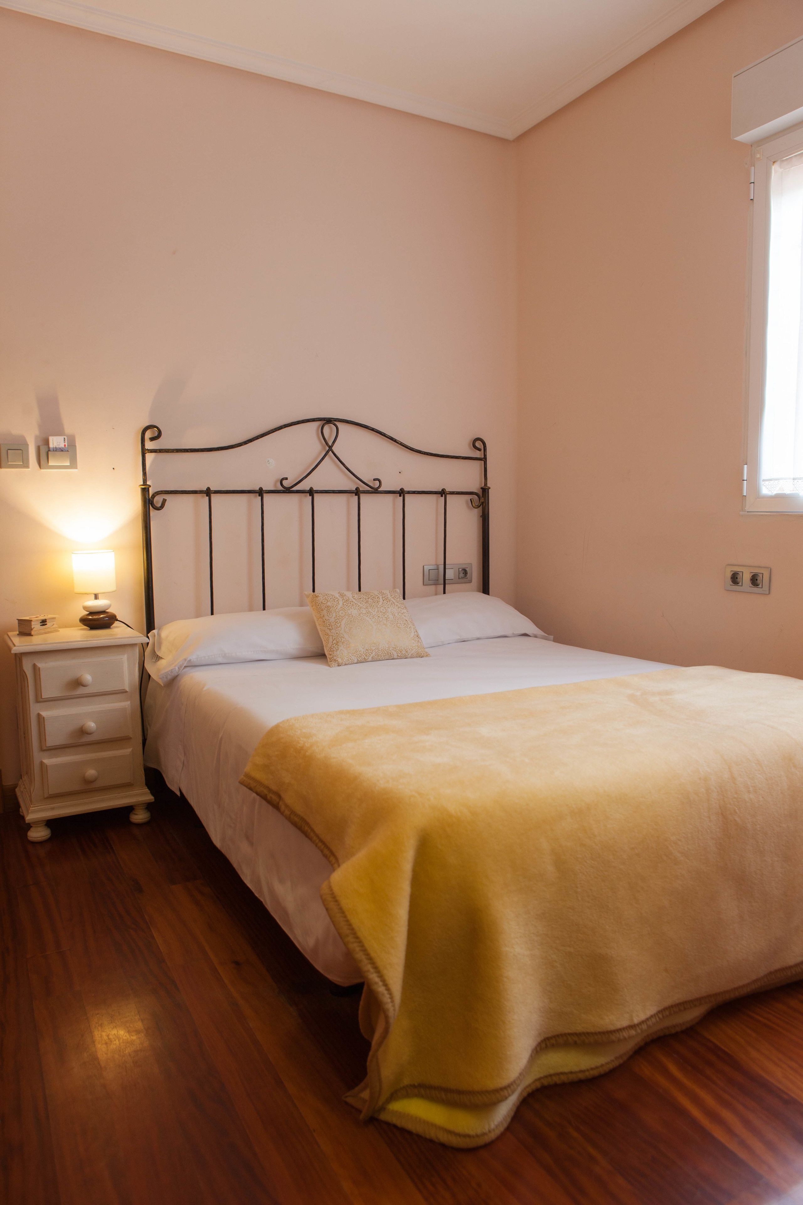 A bedroom with a bed, a nightstand, a lamp, and a window.