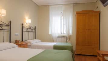 Een slaapkamer met twee bedden, een houten garderobe, een nachtkastje en een raam met dunne gordijnen.