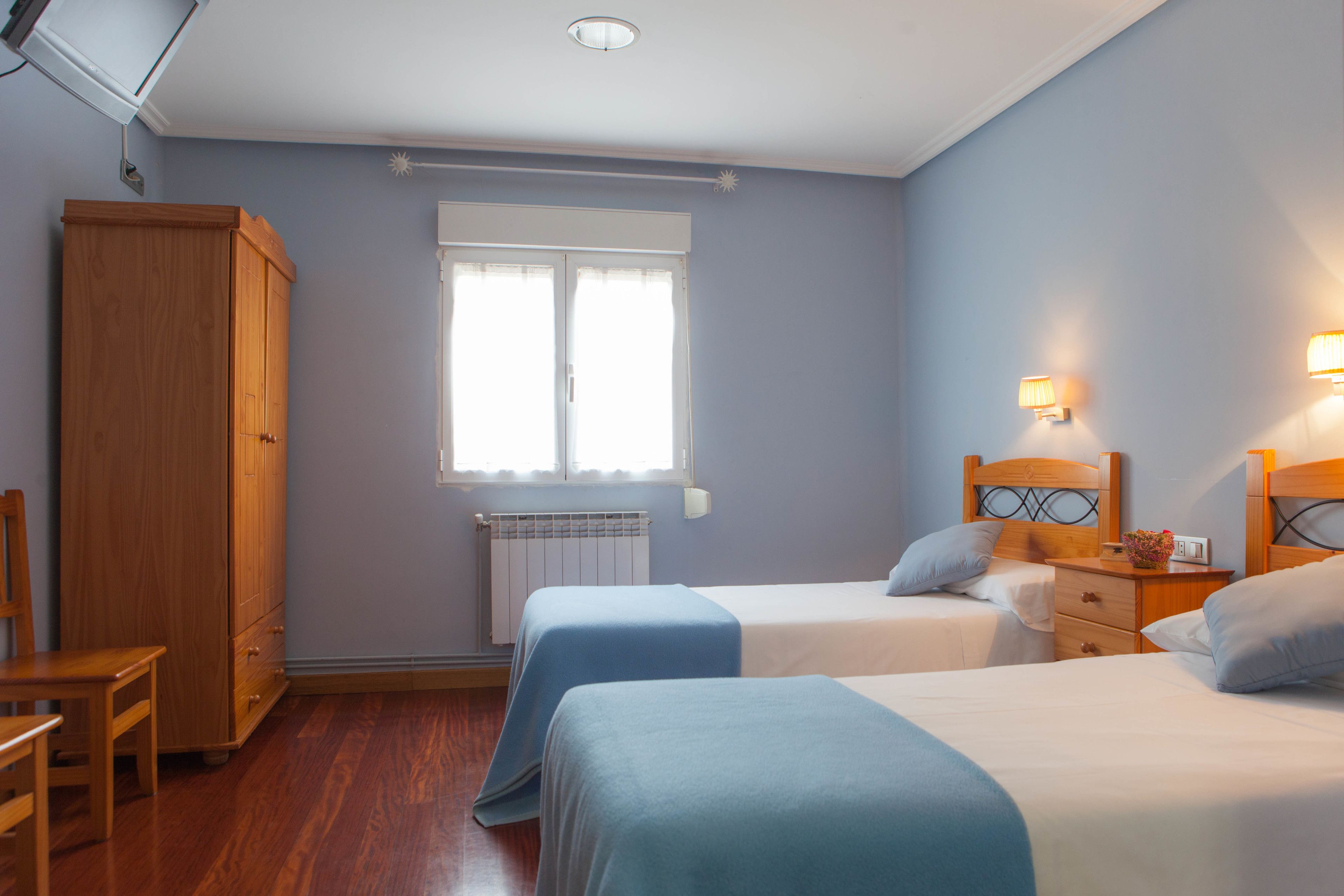 Una habitación con dos camas, un armario de madera, un radiador y una ventana con cortinas.