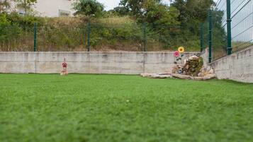 Un área verde con un muro de concreto, un pequeño comedero para pájaros y un arreglo ornamental de rocas con flores.