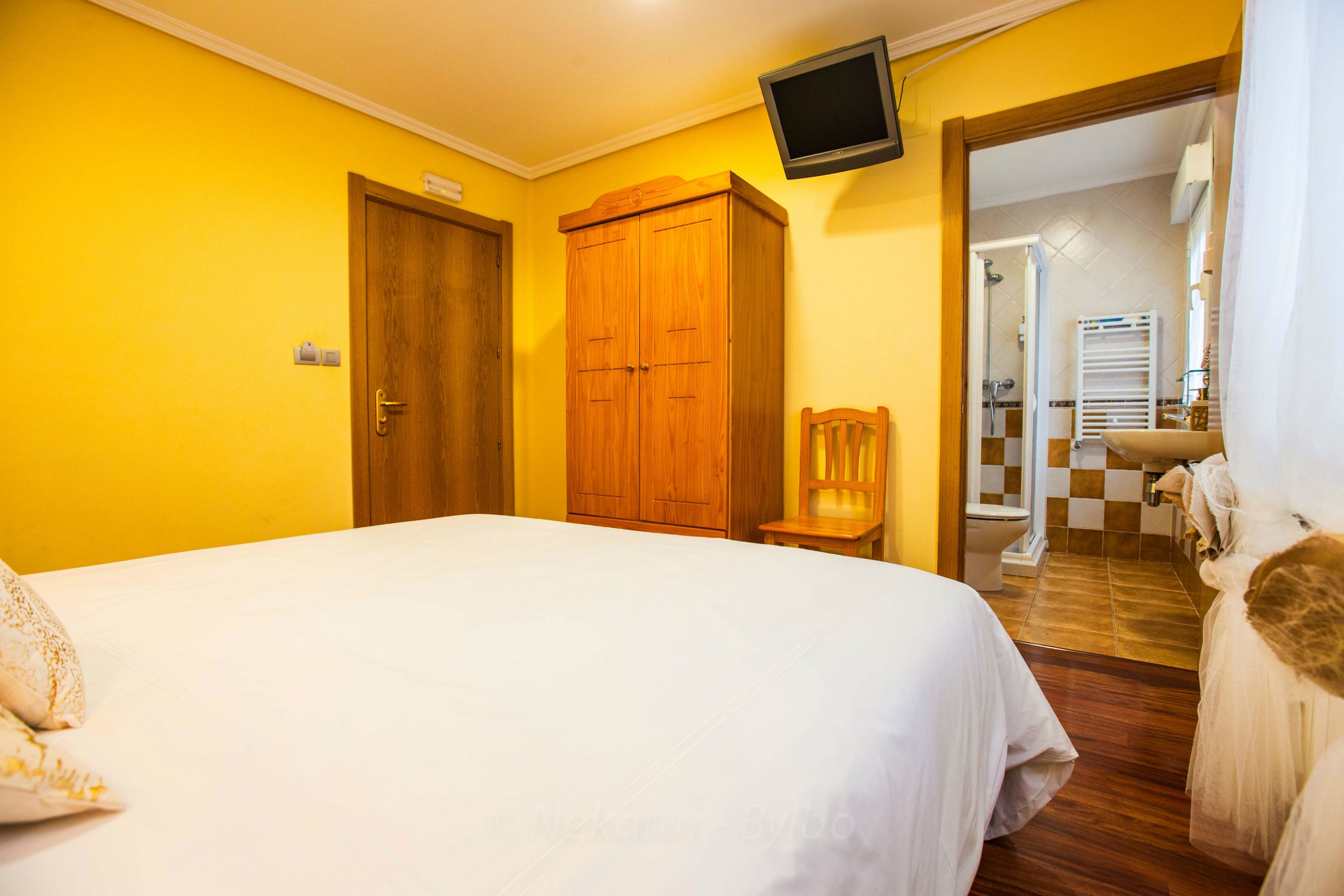 Habitació d'hotel amb llit, armari de fusta i televisió penjada a la paret.