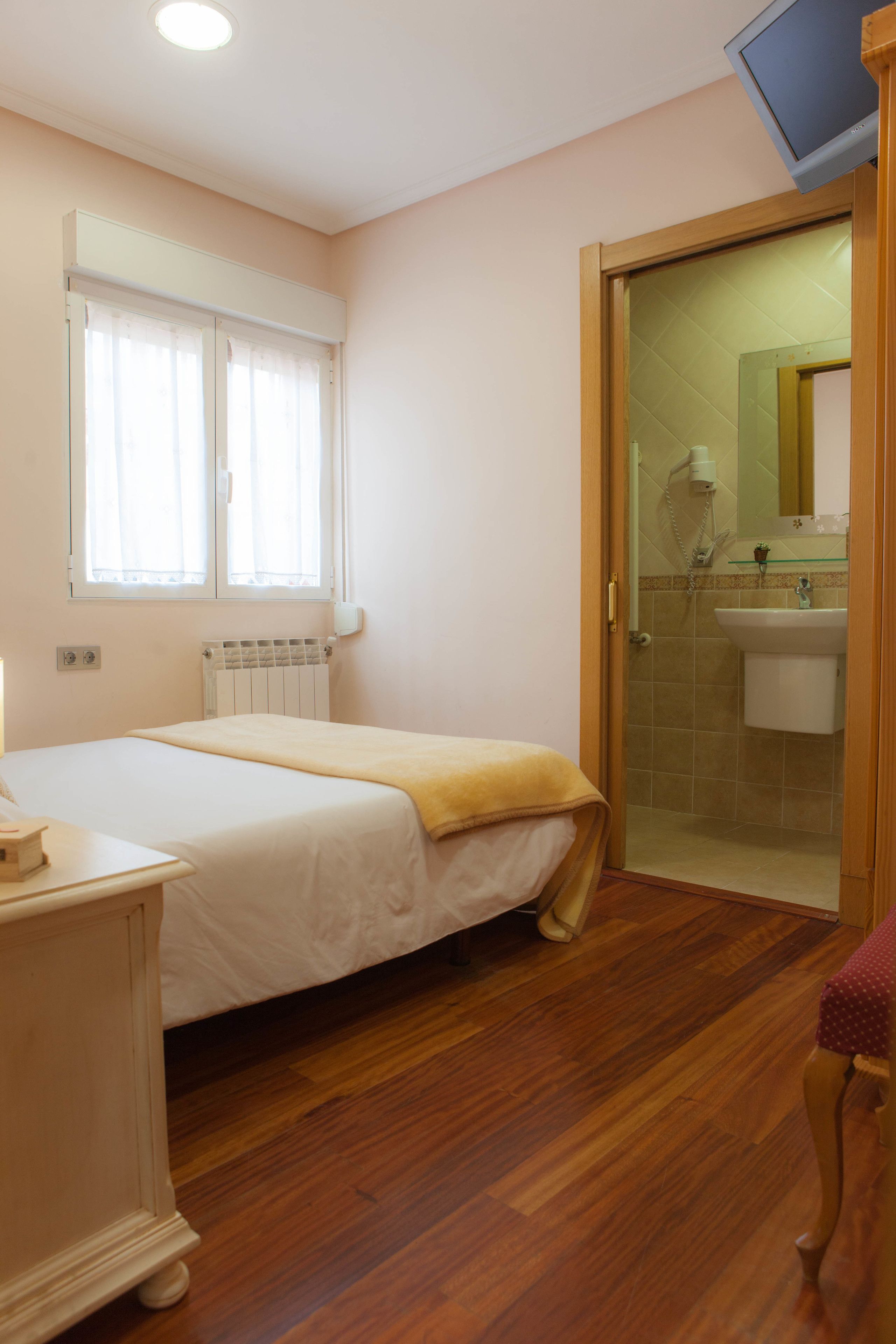 Une chambre à coucher avec un lit, une table de chevet, un plancher en bois et une salle de bain visible à travers une porte ouverte.