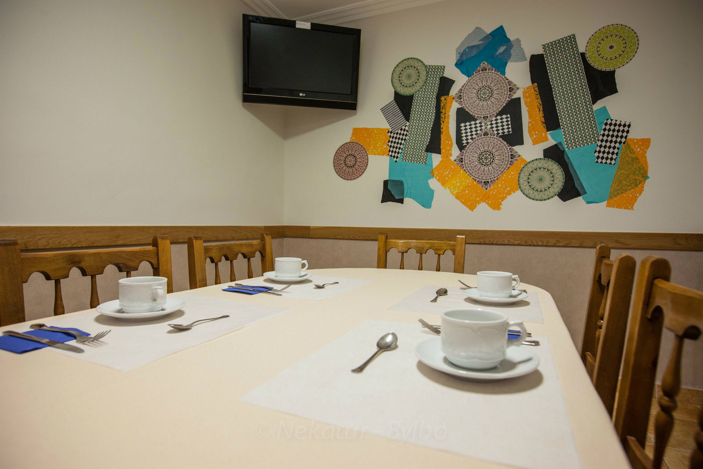 Una sala conferenze con un lungo tavolo apparecchiato per una riunione, una televisione montata a parete e una decorazione murale geometrica dai colori vivaci.