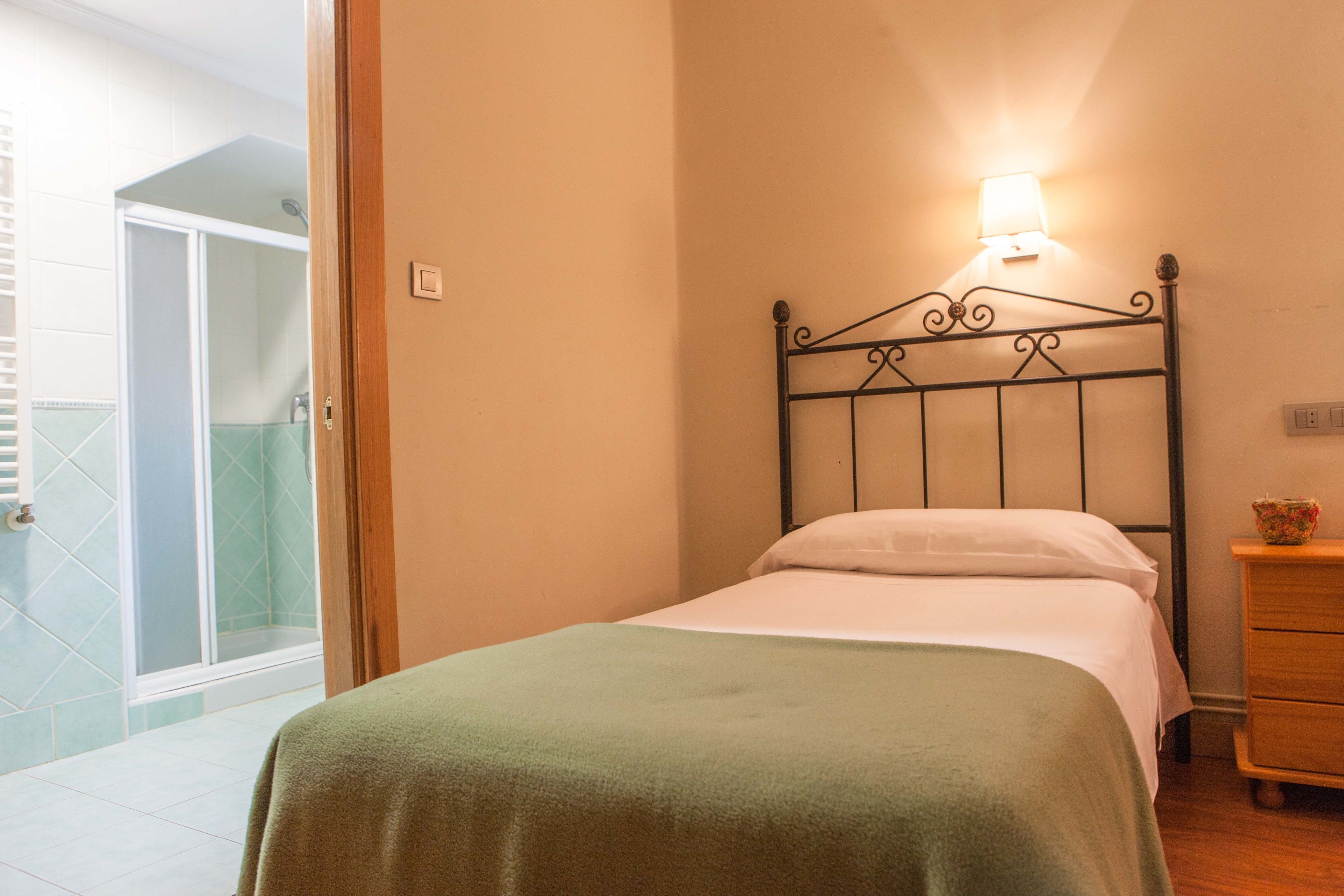 A bedroom with a bed, a nightstand, a lamp, and a view of a shower area.