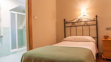 A bedroom with a bed, a nightstand, a lamp, and a view of a shower area.