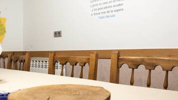 A dining table with a wooden centerpiece, wooden chairs, and a wall with a quote and chef's hat graphic.