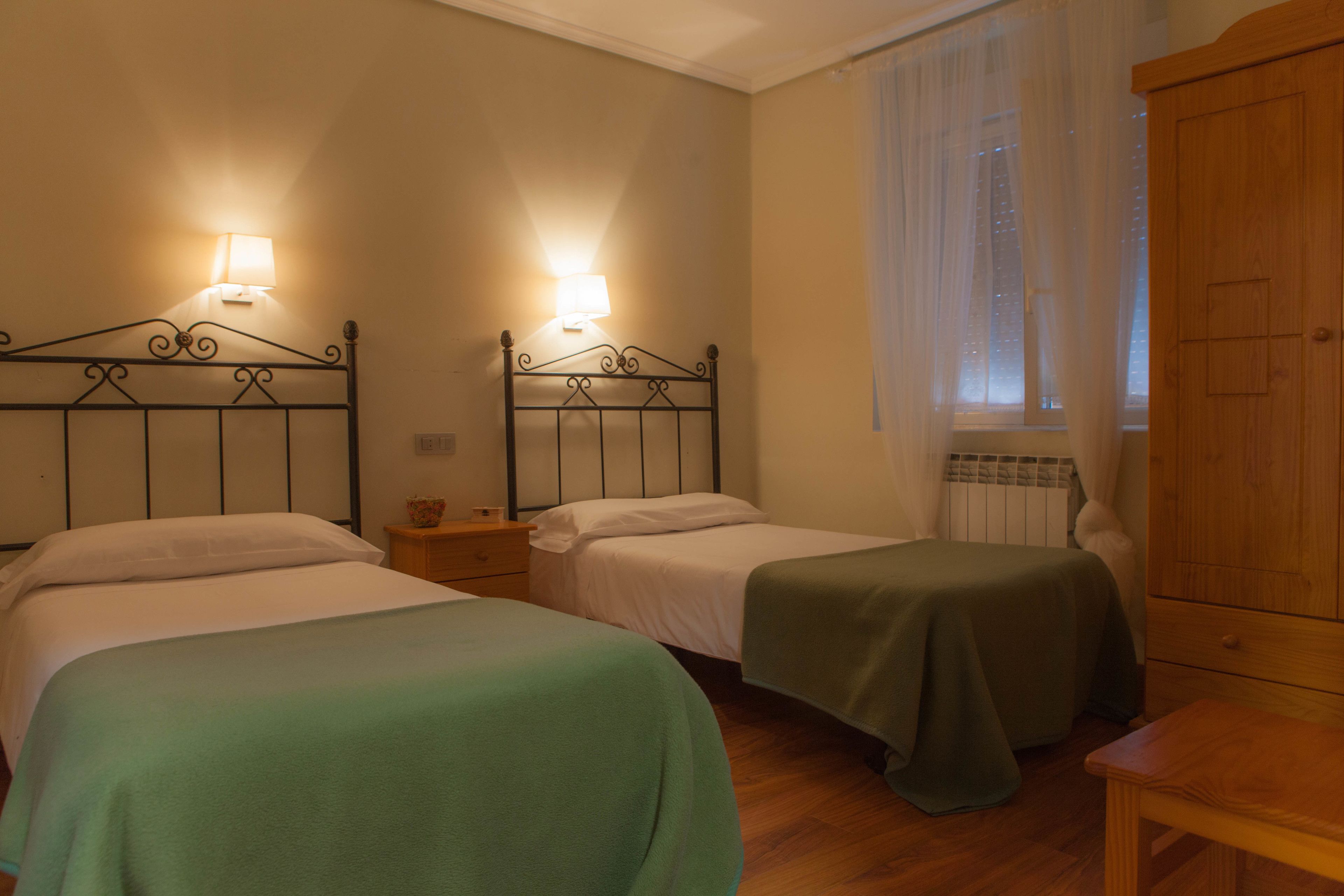 A room with two single beds, a wooden wardrobe, and a window with sheer curtains.