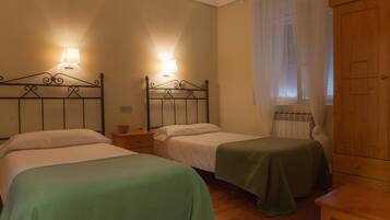 A room with two single beds, a wooden wardrobe, and a window with sheer curtains.