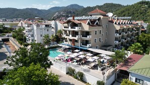 Ein mehrstöckiges Hotel mit Poolbereich auf dem Dach, Balkonen und Blick auf die umliegenden Hügel.