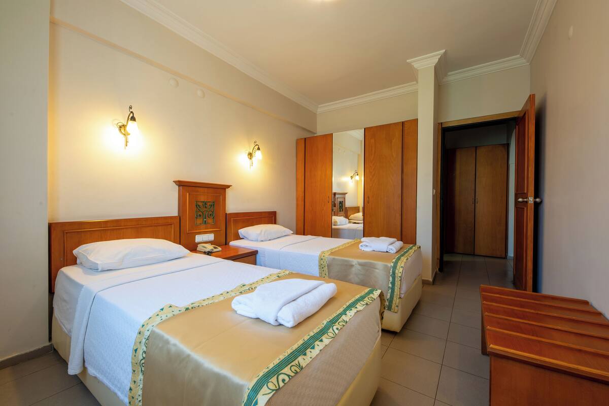 Een hotelkamer met twee bedden, een houten garderobe, een spiegel en een houten bank.