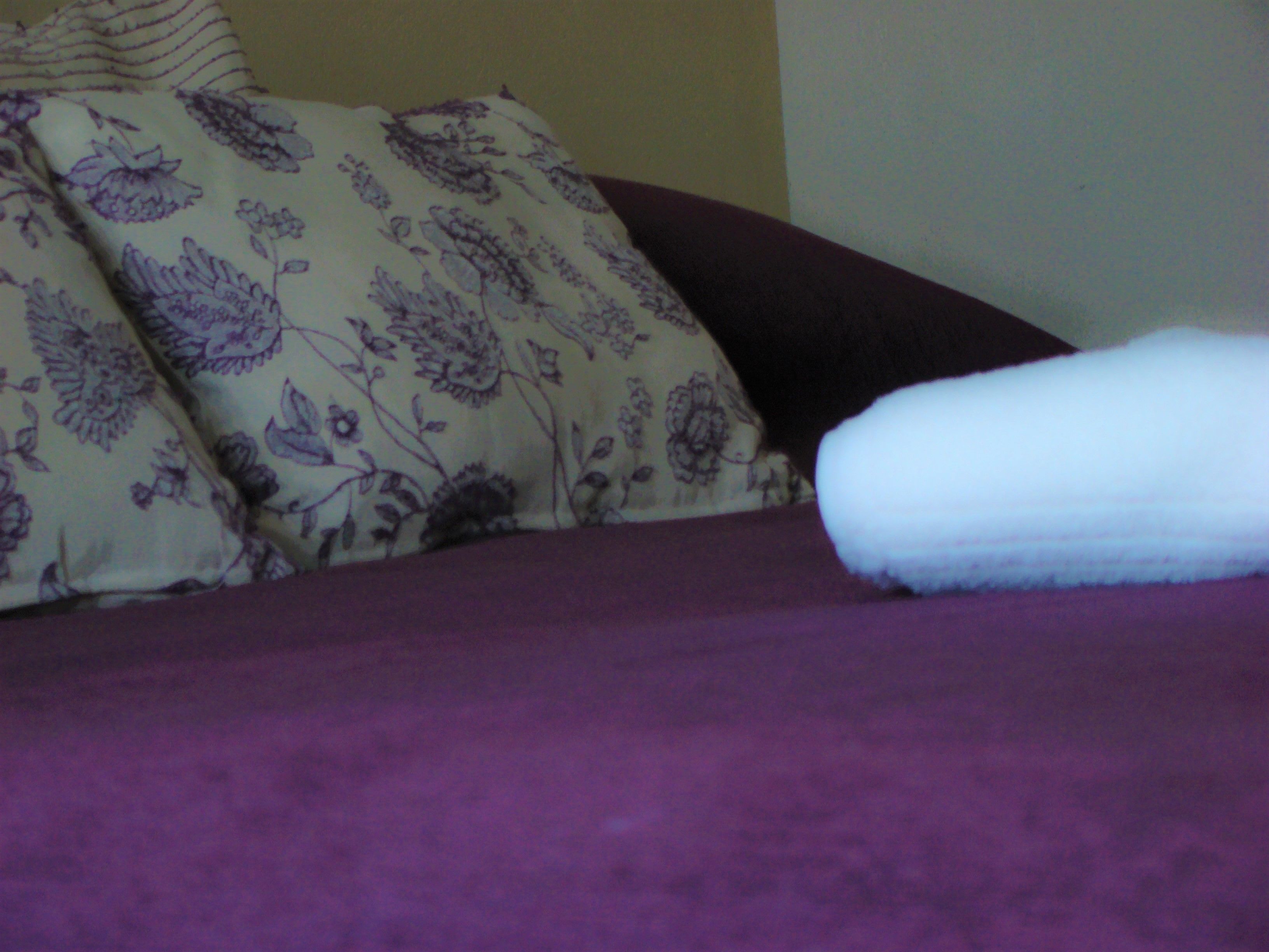 Una cama con una colcha morada y almohadas estampadas con motivos florales.