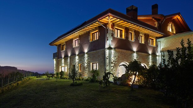 A large, multi-story house with stone walls and a well-lit facade, surrounded by a grassy lawn and trees. - Hotel Rural Gaintza (Getaria)