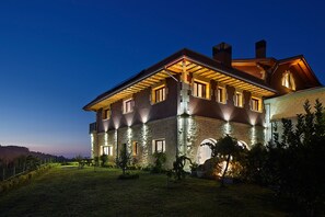A large, multi-story house with stone walls and a well-lit facade, surrounded by a grassy lawn and trees. - Hotel Rural Gaintza (Getaria)