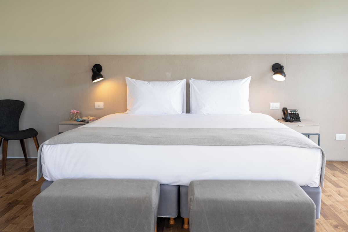 A neatly made bed with a grey blanket, two bedside lamps, a bedside phone, and a small table with a book and flowers.