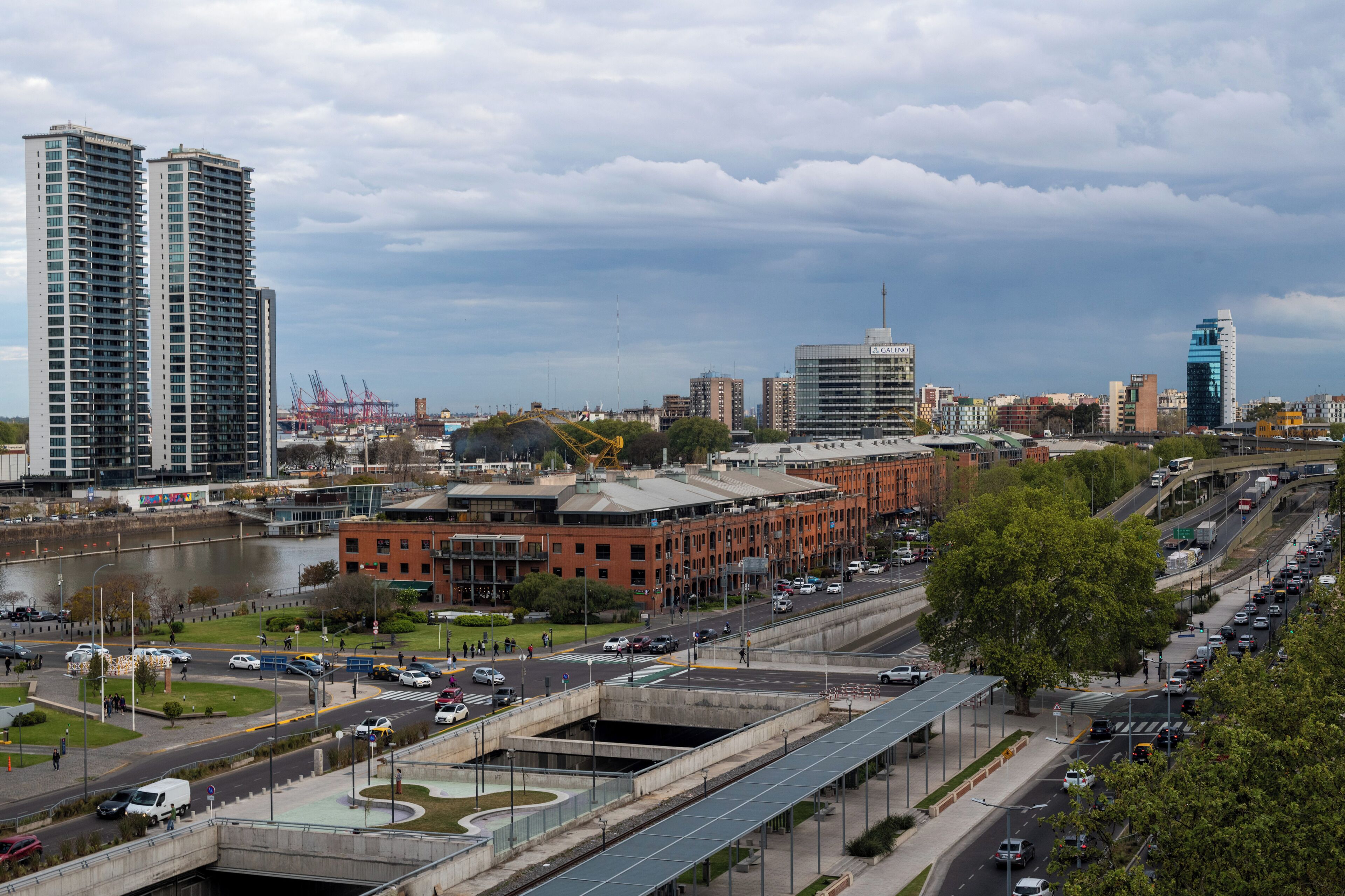 A cityscape with high-rise buildings, a river, and a busy road with vehicles.
